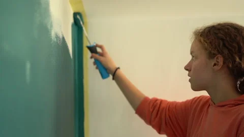 Close portrait of young curly-haired teen girl paints the wall with a roller Stock Footage 164400441
