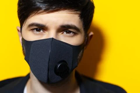 Close-up portrait of young guy wearing respiratory face mask of black color.  Stock Photos