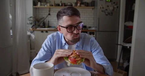 Close-up portrait of young hungry guy with pleasure eats hamburger in a cafe Video stock 157641095