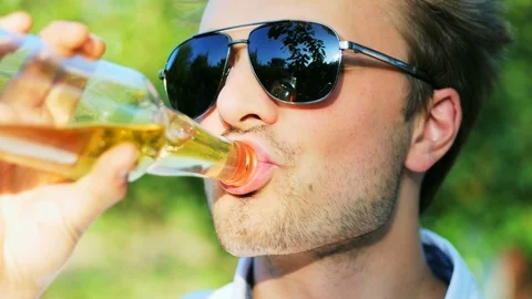 Close-up portrait of young man drinks a beer in the park Stock Footage 119989594
