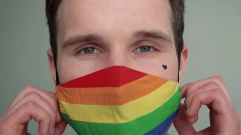 Close-up portrait of a young man taking off a rainbow face mask Vidéo 151720541