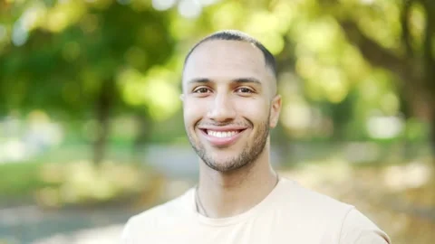 Close up portrait of a young smiling man in a t-shirt standing in a city park  Stock Footage 234876065