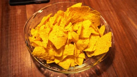 Close-up of potato chips in a transparent bowl on a wooden table and holding wit Vidéo 199512405