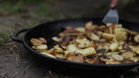 Close-up of potatoes being fried in a cast iron skillet outdoors Stock Footage 337106454