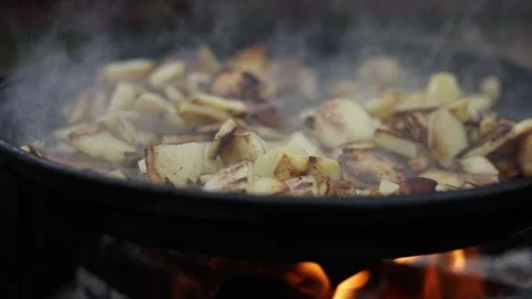 Close-up of potatoes sizzling and steaming in a cast iron skillet over an open Stock Footage 337106006