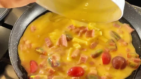 Close-Up of Pouring Beaten Eggs with Ham and Tomatoes into Frying Pan Stock Footage 343719617