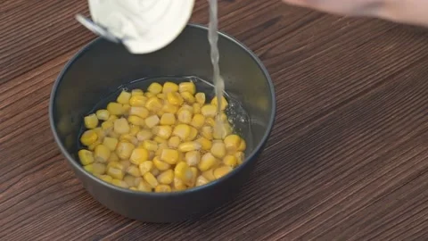 Close-up Pouring Canned yellow corn kernels into a sleek black clay bowl Stock Footage 296919815