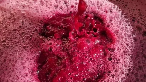Close-up pouring dark, crimson grape must, creating a deep splash in a vessel. V Stock Footage 317938614