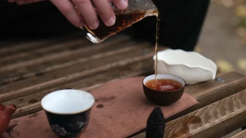 Close-up. pouring dark pu-erh tea from a glass cup into tea bowls. outdoors Stock Footage 229860826