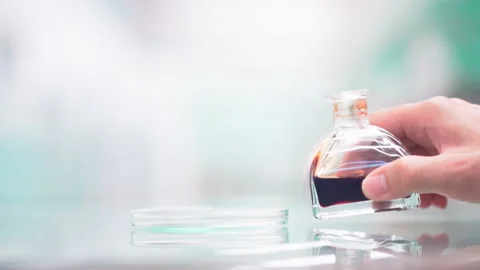 Close up pouring red brown liquid from glass bottle to flat glass container Video stock 156241291