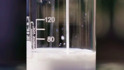 Close up pouring white emulsion to beaker bokeh background slow motion 100fps Video stock 156064293