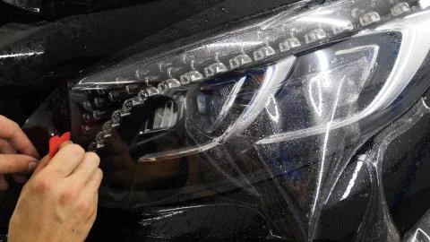 Close up to PPF installation process on a front headlight and hood. Stock Photos