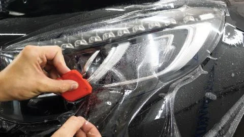 Close up to PPF installation process on a front headlight and hood. Stock Photos