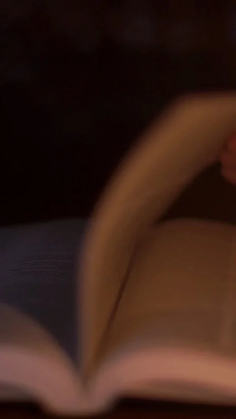 Close-up of praying hands on an open Holy Bible, turning pages in a warm dimly Vidéo 348734972