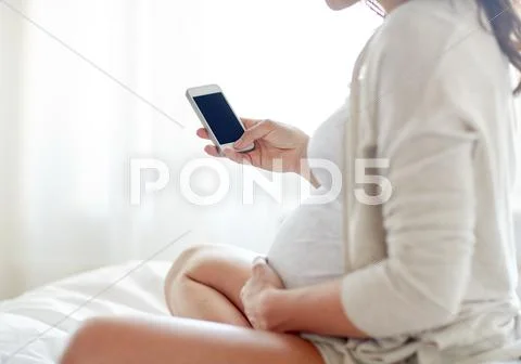 Close up of pregnant woman with smartphone in bed Stock Photos