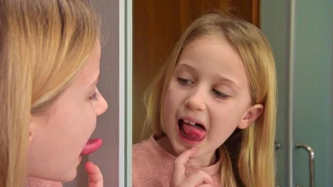 Close-up pretty eight-year-old blonde girl looks at her tongue Stock Footage 126181387