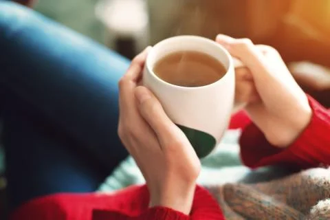 Close up of pretty woman's hands in red sweater holding cup of tea in the Stock Photos