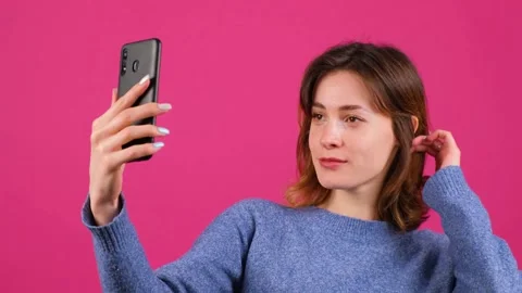 Close up of a pretty young black haired woman taking selfie on pink background. Stock Footage 153616347