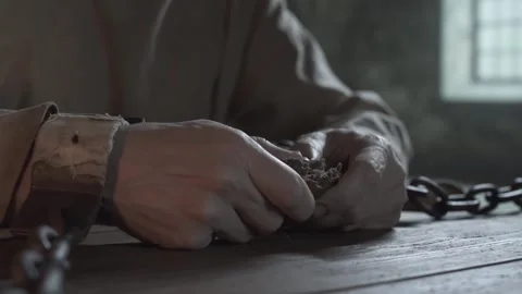 Close up of prisoner hands in chains snapping bread inside a gloomy cell Stock Footage 340502681