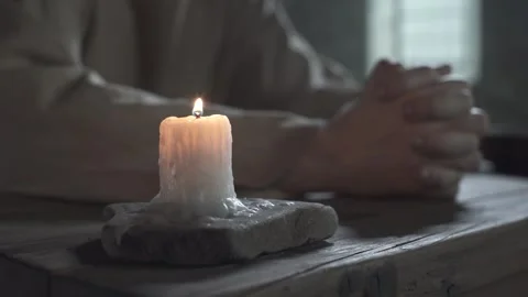 Close up of prisoner hands folded in prayer near a candle, camera tracking shot Stock Footage 340322571