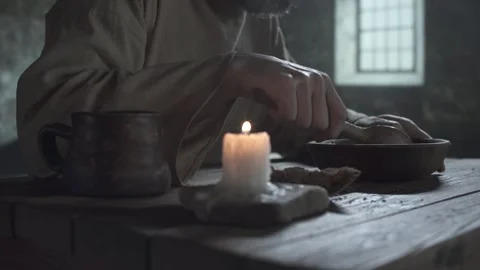 Close up of prisoner hands scooping porridge, blurred candle in foreground Stock Footage 340322617