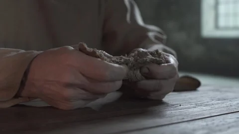 Close up of prisoner hands tearing a large loaf chunk inside a gloomy cell Stock Footage 337930155