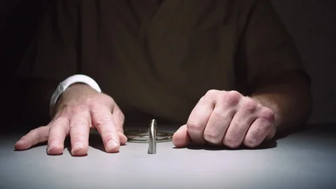 Close-up of a prisoner's hands while he sits calmly handcuffed to a table Stock Footage 99762441