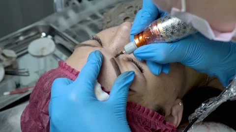 Close-up procedure microblading eyebrows. The master beautician rubs the girl's  스톡 동영상 99869341