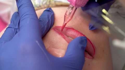 Close up process of applying permanent makeup tattoo of red on lips woman in bea Stock Footage 168199282