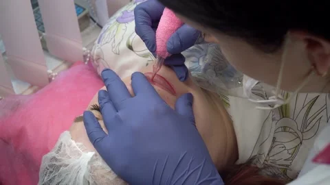 Close up process of applying permanent makeup tattoo of red on lips woman in Stock Footage 234909122