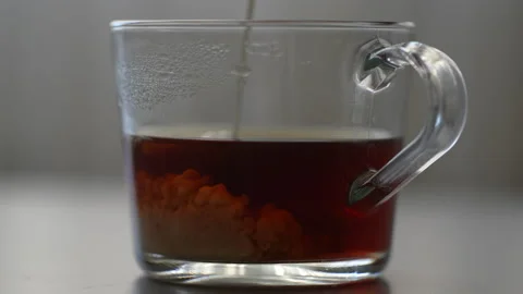 Close-up process pouring milk into glass cup of coffee creating swirling blend Stock Footage 297632438
