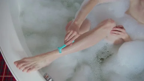 Close up process of removing hair with blue razor from leg covered in soapy foam Stock Footage 130754497