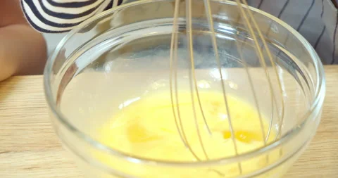 Close-up process of whipping eggs with a whisk in a transparent bowl Stock Footage 131875675