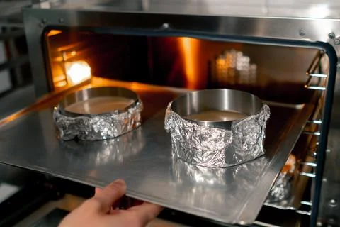 Close up in a professional kitchen a baker inserts a baking tray with cake molds Stock Photos