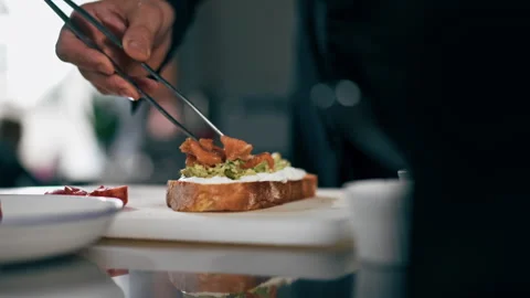 Close up in a professional kitchen a chef in a black jacket puts salmon on toast Stock Footage 276871783