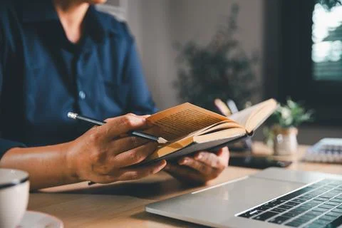 Close-up of a professional reading an open book and holding a pencil beside.. Stock Photos