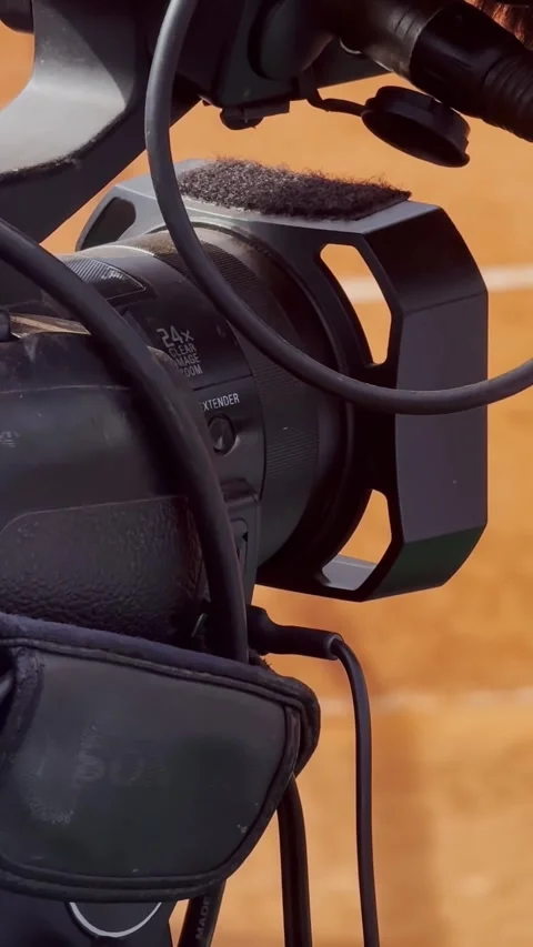Close-up of a professional video camera and cable beside a clay tennis court Stock Footage 336839941