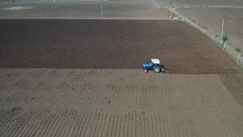 Close profile drone tracking shot of a blue tractor machine driver working on Stock Footage 337225759