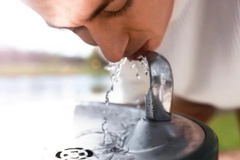 Close-up profile of a man drinking fresh water from an outdoor public drink.. Foto stock