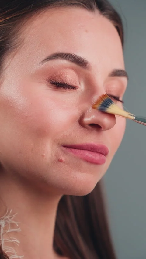 Close-up profile of visagist applying cosmetics to young woman's skin with .. Stock Footage 332660899