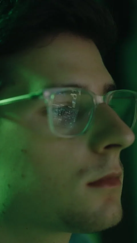Close-up profile of a young male editor working at night, with code reflecting Stock Footage 344166861