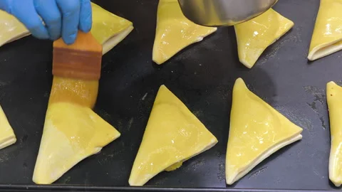 Close-up of puff pastry turnovers being brushed with egg wash for a golden Stock Footage 339286180