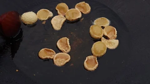 Close-up of puffed rice snacks being fried in hot oil with a wooden spoon nearby Stock Footage 338430800