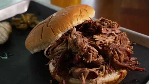Close-Up Pulled Pork BBQ Sandwich Plate with Pinto Beans and Pickles in Rustic Stock Footage 346249441