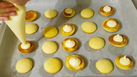 Close up of putting white cream on small baked cookies with piping bag Stock Footage 327259112