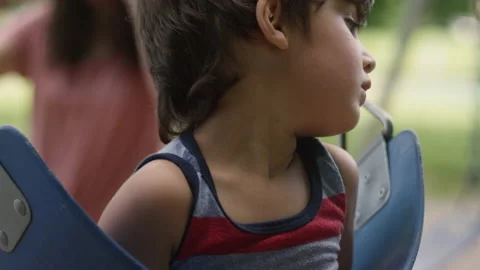 Close-up rack focus of a mother watching her son swing in a park swing Stock-Footage 143633572