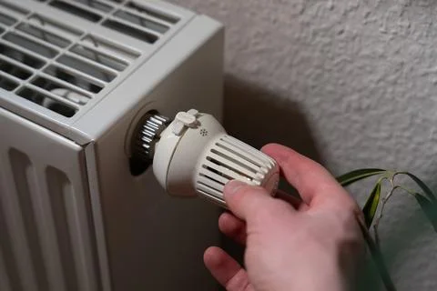 Close-up of a radiator, a hand is setting the lowest level of energy 写真素材