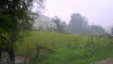 Close-up of rain and droplets through glass overlooking green nature with cloudy Stock Footage 218586167