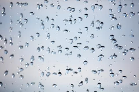 Close-up of rain droplets on transparent surface with soft sky background Stock Photos