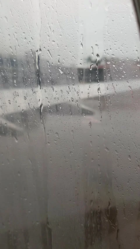 Close-up of raindrops on airplane window with blurred airport view Stock Footage 327247408